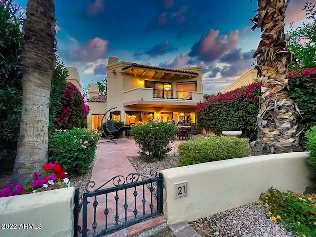 back house at dusk featuring a balcony and a patio