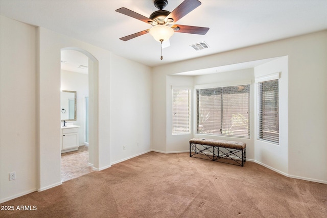 empty room featuring arched walkways, visible vents, light carpet, ceiling fan, and baseboards