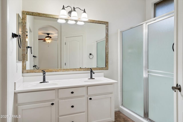 full bath with double vanity, a stall shower, ceiling fan, and a sink