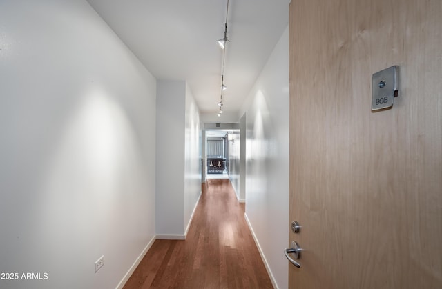 corridor featuring baseboards, track lighting, and wood finished floors