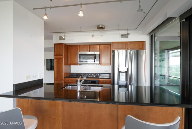 kitchen featuring visible vents, brown cabinetry, rail lighting, stainless steel appliances, and a sink