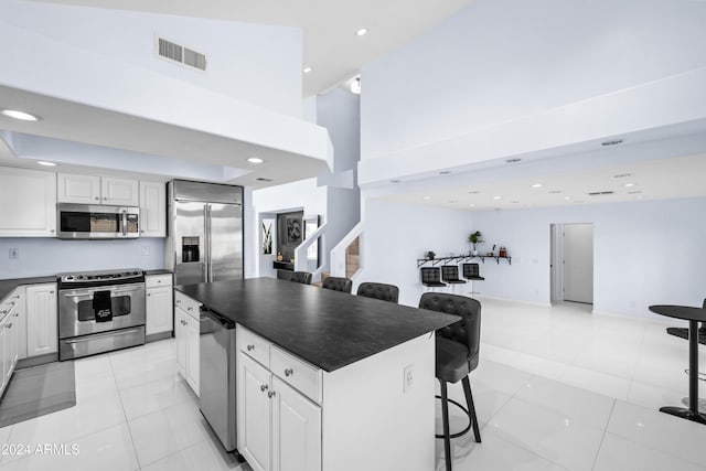 kitchen with stainless steel appliances, dark countertops, a breakfast bar area, white cabinets, and a high ceiling