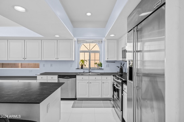 kitchen featuring appliances with stainless steel finishes, dark countertops, a sink, light tile patterned flooring, and recessed lighting