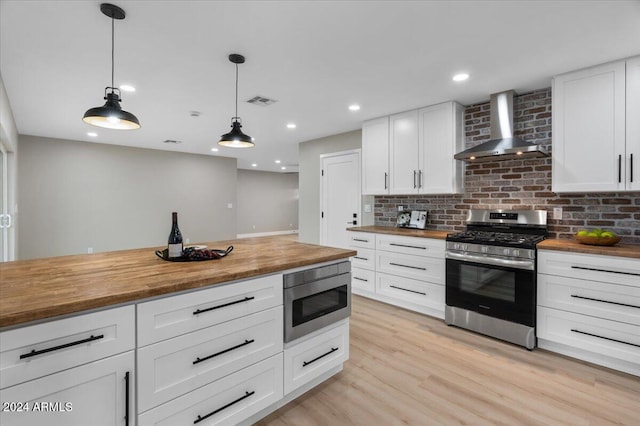 kitchen with white cabinets, stainless steel appliances, butcher block countertops, and wall chimney exhaust hood