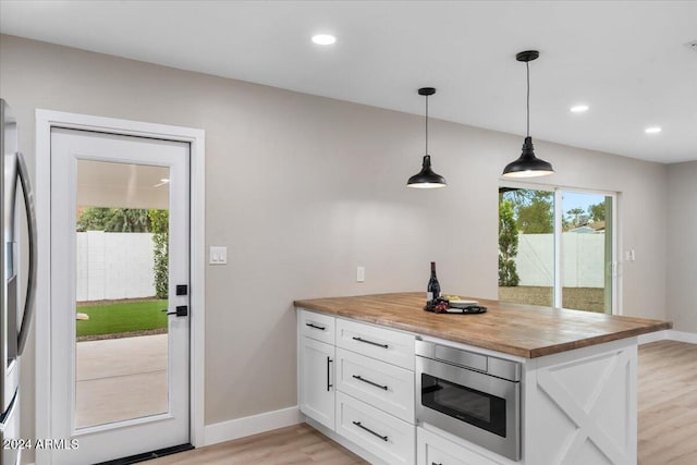 kitchen featuring appliances with stainless steel finishes, wooden counters, decorative light fixtures, white cabinets, and light wood-type flooring