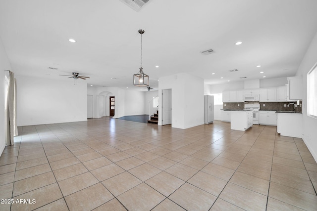 unfurnished living room with arched walkways, light tile patterned floors, a sink, and visible vents