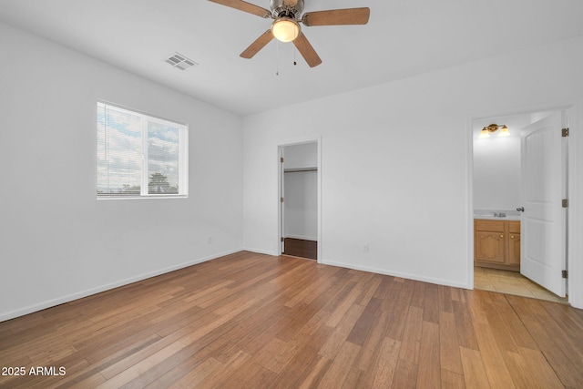 unfurnished bedroom with visible vents, light wood-style flooring, baseboards, and a spacious closet