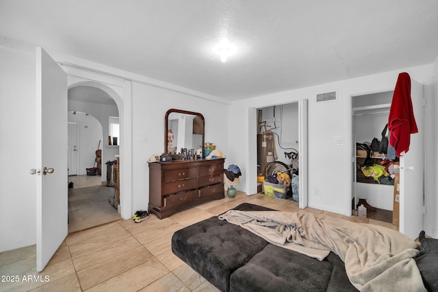 bedroom with arched walkways, electric water heater, visible vents, and light tile patterned floors