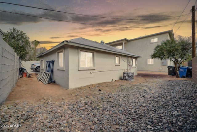 back of property at dusk featuring central air condition unit, fence, and stucco siding