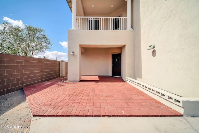 entrance to property featuring a balcony, stucco siding, fence, and a patio