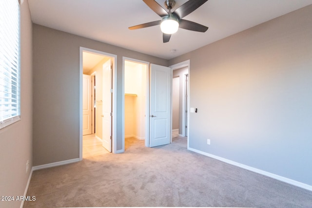 unfurnished bedroom featuring ceiling fan, light colored carpet, a closet, and a walk in closet