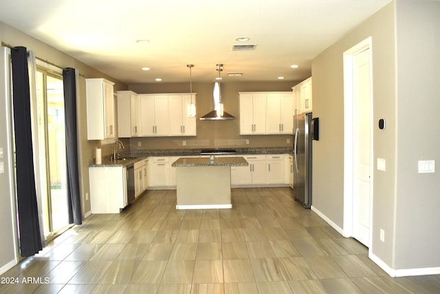 kitchen featuring appliances with stainless steel finishes, pendant lighting, a center island, sink, and wall chimney range hood