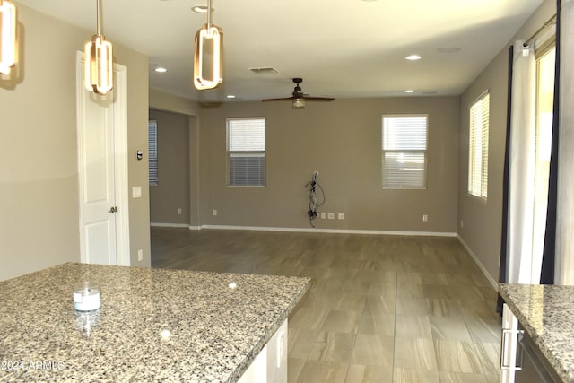 kitchen with light stone counters, hanging light fixtures, and ceiling fan