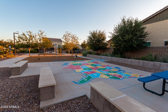 pool at dusk featuring a patio area and a playground