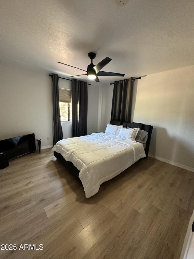 bedroom with a textured ceiling, a ceiling fan, baseboards, and wood finished floors