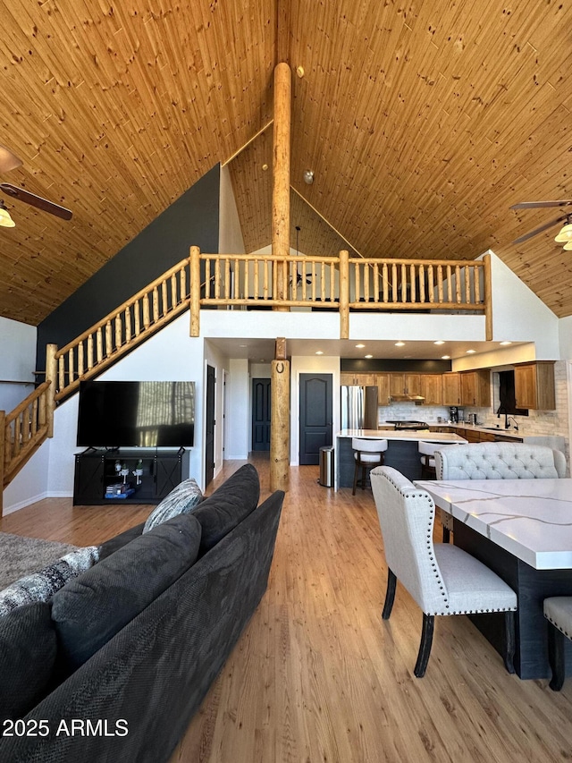 living area with light wood-type flooring, high vaulted ceiling, a ceiling fan, stairway, and wood ceiling