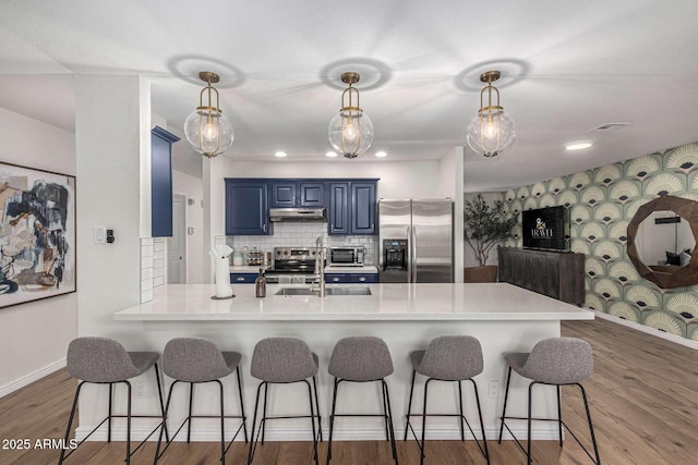 kitchen with sink, blue cabinetry, appliances with stainless steel finishes, decorative light fixtures, and kitchen peninsula