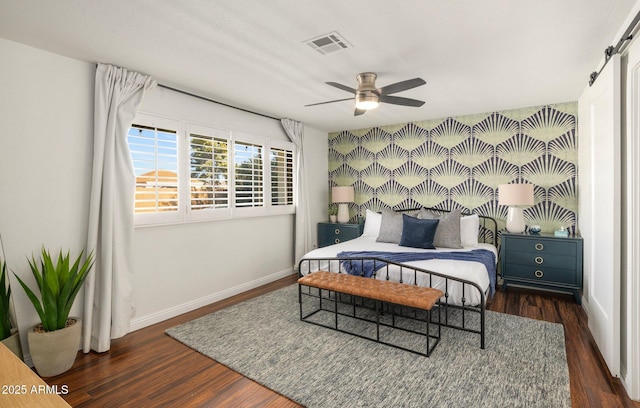 bedroom featuring dark wood-type flooring, ceiling fan, and a barn door