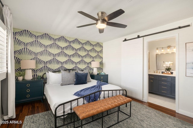 bedroom with dark hardwood / wood-style floors, a barn door, ceiling fan, and ensuite bathroom