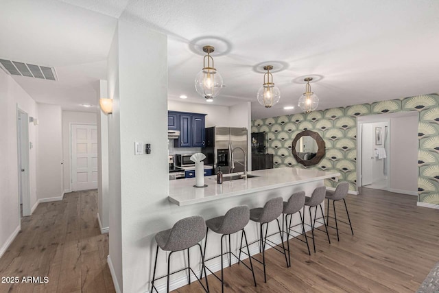 kitchen with blue cabinets, sink, a kitchen bar, kitchen peninsula, and stainless steel refrigerator with ice dispenser