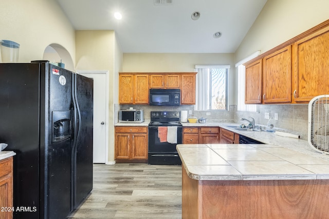 kitchen with black appliances, sink, vaulted ceiling, decorative backsplash, and light hardwood / wood-style floors