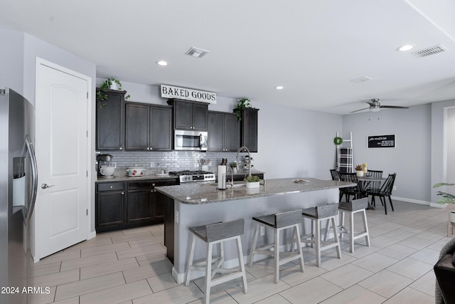 kitchen with appliances with stainless steel finishes, backsplash, a kitchen island with sink, ceiling fan, and a breakfast bar area