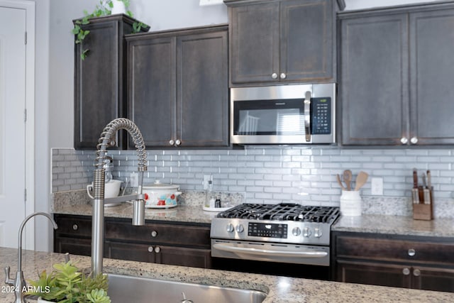 kitchen featuring decorative backsplash, dark brown cabinets, stainless steel appliances, and light stone counters