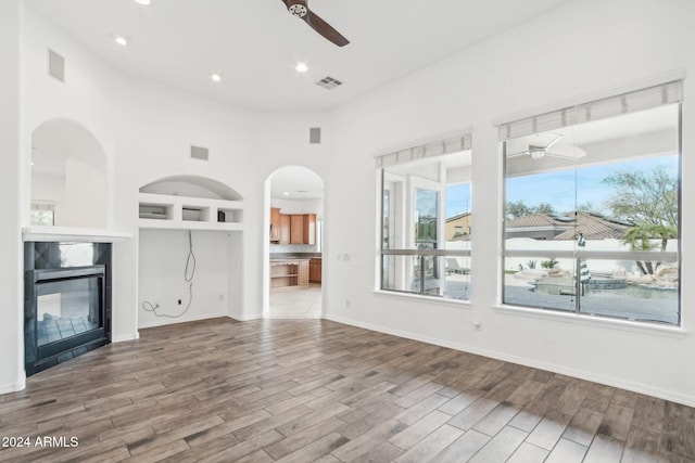 unfurnished living room featuring built in shelves, a towering ceiling, light hardwood / wood-style flooring, and a wealth of natural light