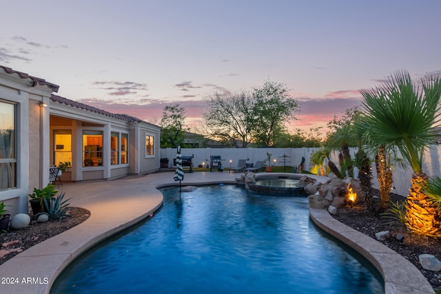 pool at dusk featuring an in ground hot tub and a patio