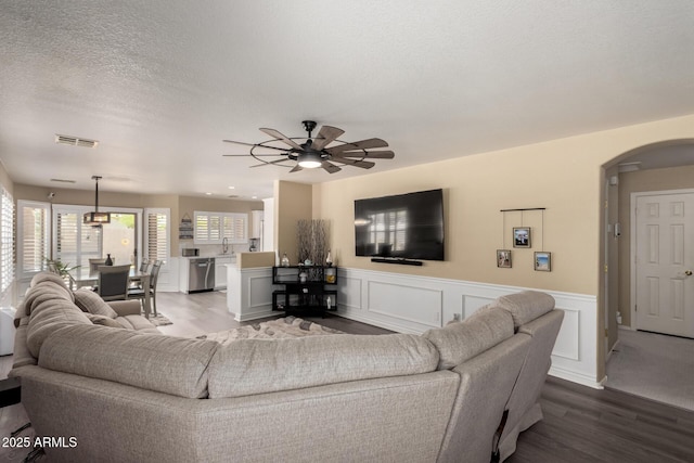 living room featuring a textured ceiling, a ceiling fan, visible vents, arched walkways, and wood finished floors