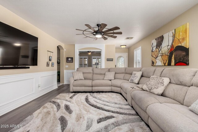 living area featuring visible vents, arched walkways, a ceiling fan, wainscoting, and wood finished floors