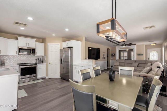 dining room with arched walkways, dark wood-style flooring, visible vents, and recessed lighting