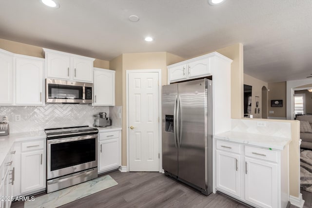 kitchen featuring white cabinets, appliances with stainless steel finishes, arched walkways, and decorative backsplash
