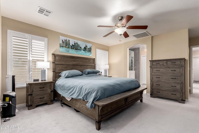 bedroom featuring arched walkways, ensuite bath, visible vents, and light colored carpet