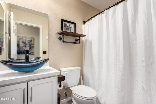 bathroom featuring toilet, vanity, and a textured wall