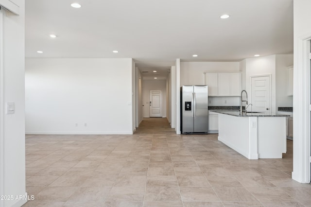 kitchen with sink, white cabinetry, a center island with sink, dark stone countertops, and stainless steel fridge