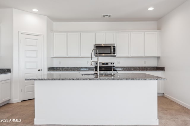 kitchen featuring dark stone countertops, appliances with stainless steel finishes, a kitchen island with sink, and white cabinets