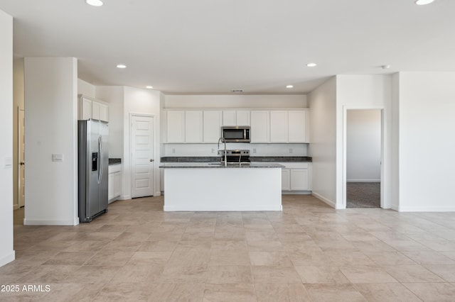 kitchen featuring stainless steel appliances, a kitchen island with sink, dark stone countertops, and white cabinets