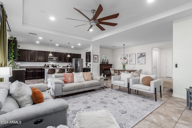 tiled living room featuring ceiling fan with notable chandelier and a tray ceiling