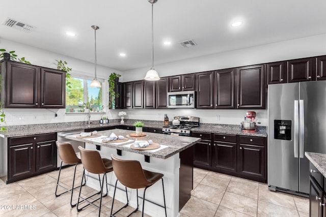 kitchen with a kitchen island, pendant lighting, stainless steel appliances, a kitchen bar, and dark brown cabinets