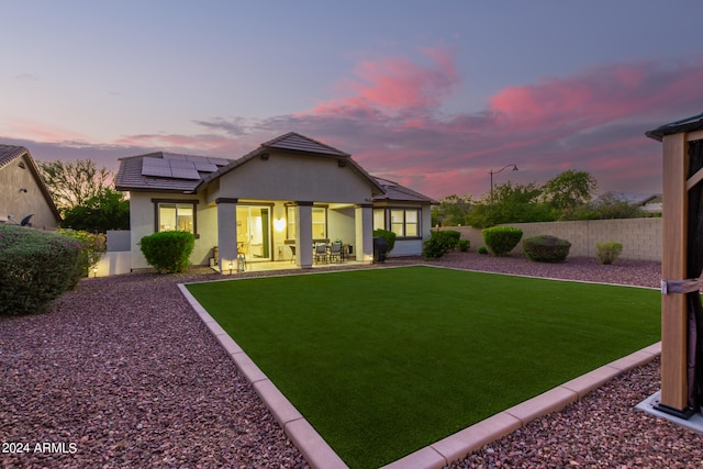 back house at dusk featuring solar panels, a lawn, and a patio area