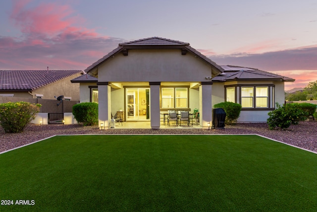 back house at dusk with a lawn and a patio