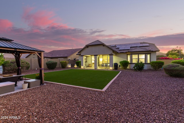 back house at dusk with solar panels, outdoor lounge area, a patio area, and a gazebo