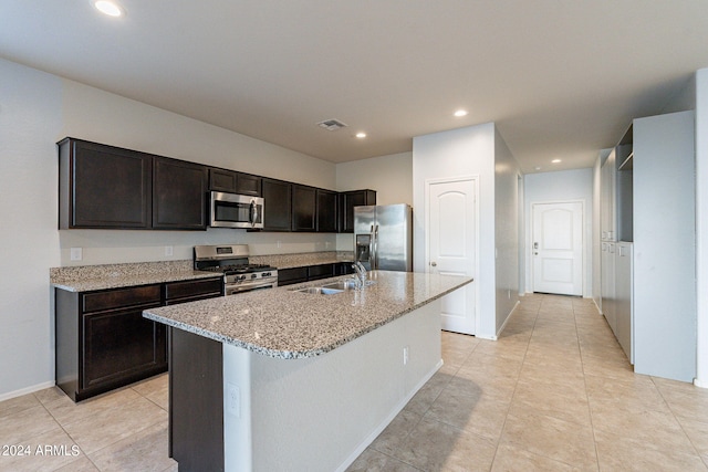 kitchen featuring a kitchen island with sink, dark brown cabinetry, light stone counters, sink, and stainless steel appliances