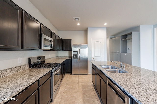 kitchen with light stone countertops, dark brown cabinetry, sink, appliances with stainless steel finishes, and light tile patterned floors