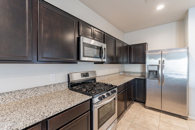 kitchen featuring light stone countertops, light tile patterned floors, appliances with stainless steel finishes, and dark brown cabinetry