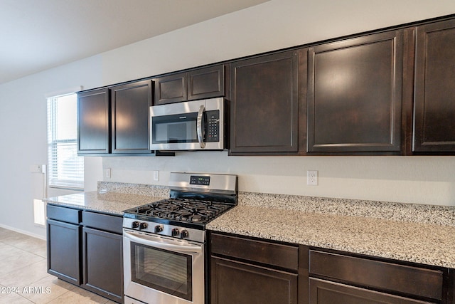 kitchen with dark brown cabinetry, light stone countertops, appliances with stainless steel finishes, and light tile patterned floors