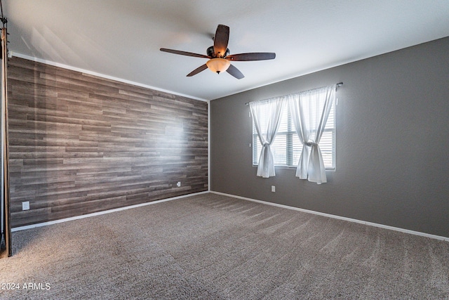 spare room featuring dark colored carpet, ceiling fan, and wood walls