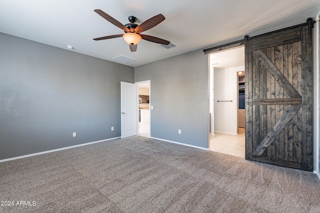 unfurnished bedroom with ceiling fan, light colored carpet, and a barn door