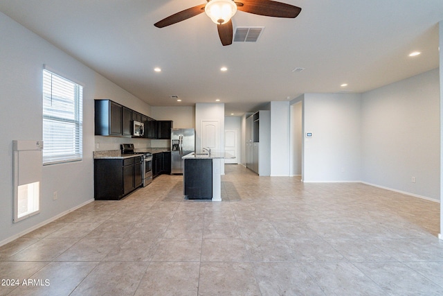 kitchen featuring a kitchen island with sink, ceiling fan, sink, light stone counters, and stainless steel appliances